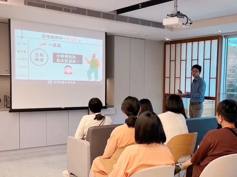 張凱翔醫師站在投影幕旁講解生長曲線，投影片寫著小時候的胖長大就是胖，台下媽媽們坐著聆聽