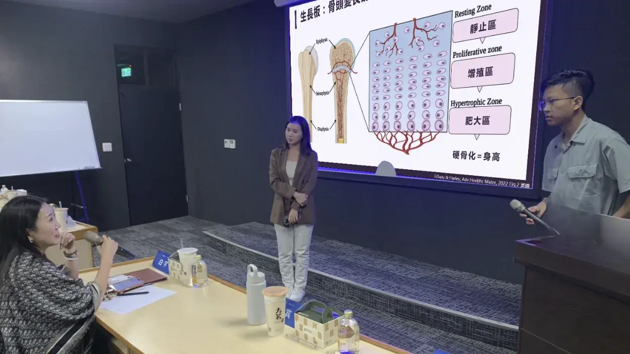 張凱翔醫師站在講台旁,投影幕上是生長板的構造圖,前排來賓拿著麥克風說話