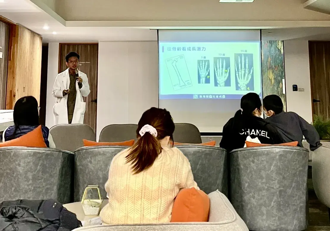 張凱翔醫師在診所講座空間演講，投影片寫著從骨齡看成長潛力，家長坐在沙發上聆聽