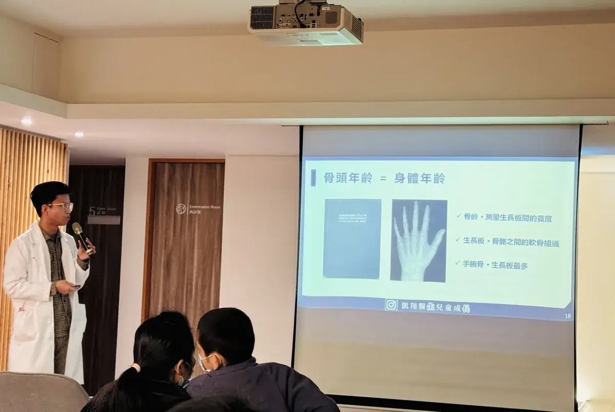 張凱翔醫師穿著白袍拿麥克風演講，投影片講解骨頭年齡，台下家長坐著聆聽