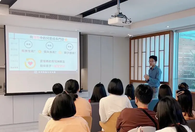張凱翔醫師站在投影幕旁演講，投影片寫著我理想中的兒童成長門診，台下媽媽們坐著聆聽